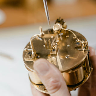 Close-up of a person adjusting the gears of a mechanical clock.